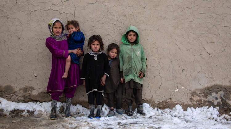 Jungen und Mädchen stehen an einer Wand und schauen in die Kamera. Auf dem Boden liegt Schnee.