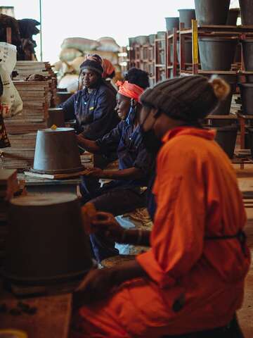 Women making clay filters in Uganda, smiling.