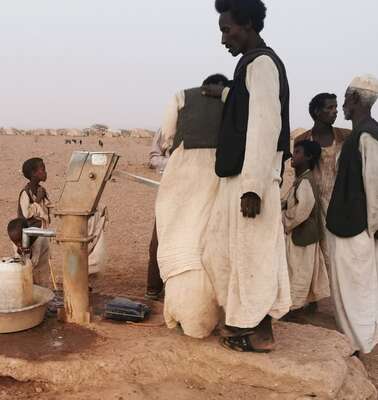 In einer wüstenartigen Landschaft umstehen Männer einen Zapfhahn für Wasser.