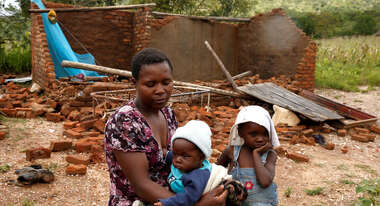 A woman and her children sitting in front of a house destroyed by cyclone Idai