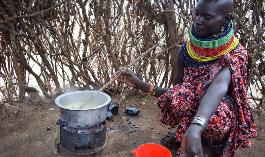 Eine Frau hockt an einer Feuerstelle in einer Hütte und kocht.