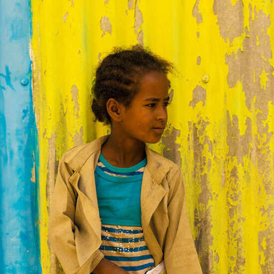 Mädchen mit Schulmappe vor blau-gelber Wand