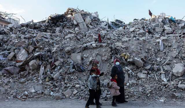 Eine Familie im türkischen Hatay steht nach den Erdbeben 2023 vor großen Trümmerbergen.