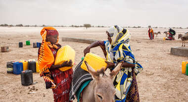 Zwei Frauen heben gelbe Kanister auf einen Esel.