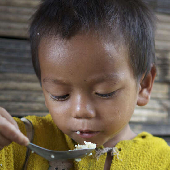 Ein kleiner Junge isst Reis aus dem Topf