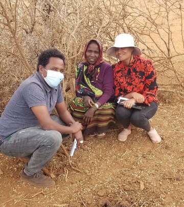 Drei Personen posieren in Hocke auf einem Feld und lächeln in die Kamera.