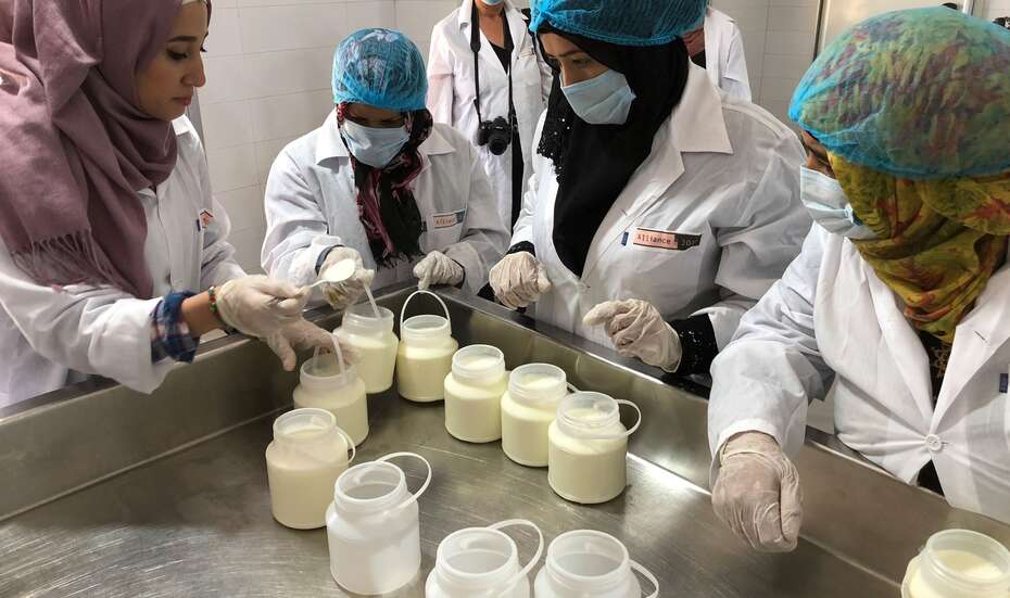 Vier Frauen in Schutzkleidung stehen an einem Tisch und begutachten Joghurt.