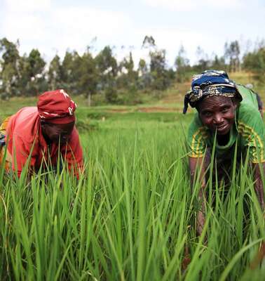 Two women stand bent over on a field, one looks smiling into the camera.