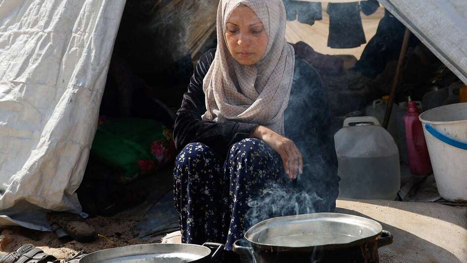 Famine in Gaza: A woman sits in front of two pots while cooking