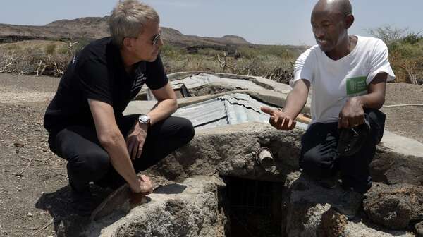 Till Wahnbeck und Einheimischer knieen vor einem Rohr im Boden