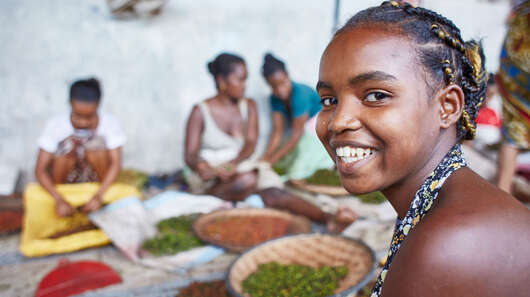 Mädchen und Frauen arbeiten in einer Pfefferfabrik, ein Mädchen im Vordergrund lächelt in die Kamera