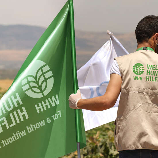 Man with WHH branded jacket holds flag with WHH logo