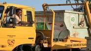 Ein Fahrer schaut aus dem Fenster eines LKW mit Müllcontainer.
