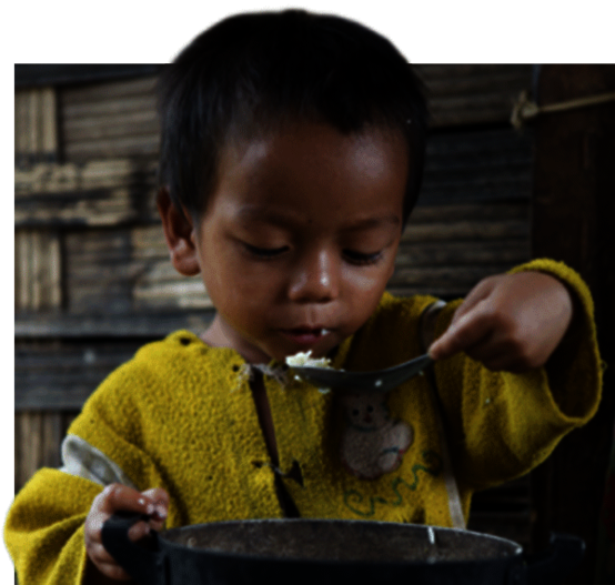Ein Junge sitzt vor einem Topf und löffelt Reis.