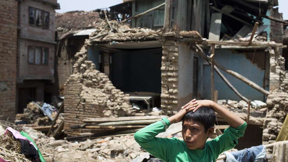A boy in the front. Behind him a destroyed house.