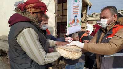 Ein Mitarbeiter einer Hilfsorganisation übergibt in Folie verpackte Brote an einen Mann