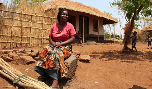 Frau sitzt vor Hütte auf einem Hocker