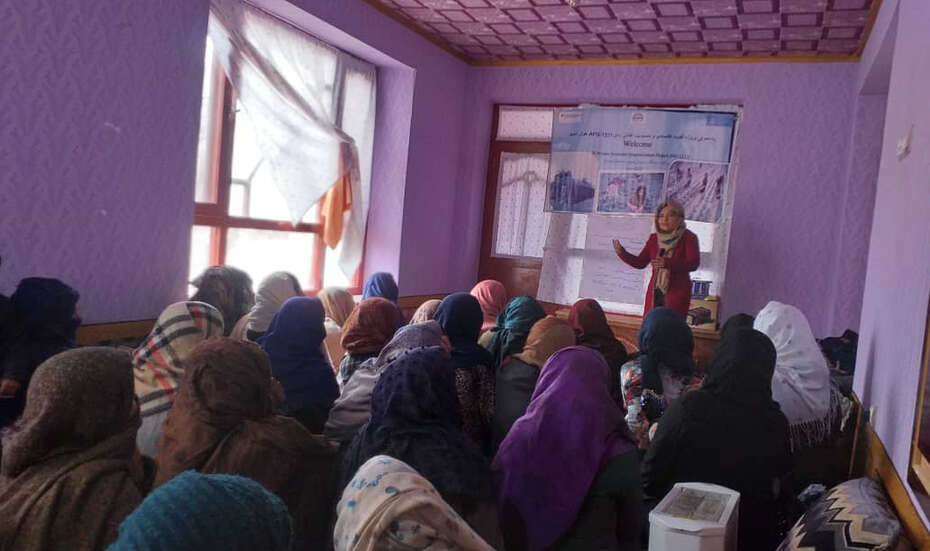 Viele Frauen sitzen in einem Raum, vorne steht eine Person und unterrichtet.