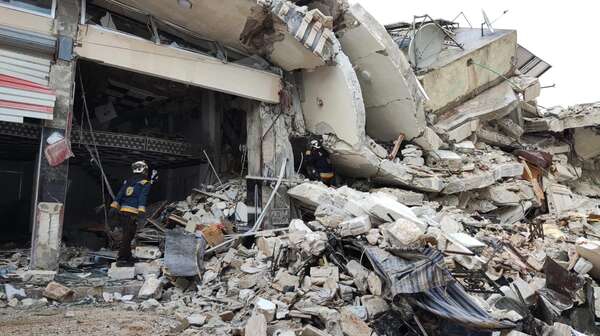 Zwei Männer in Schutzkleidung vor einem zerstörten Gebäude.