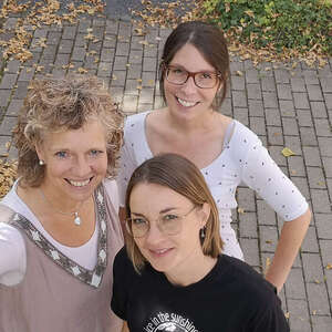 Drei Frauen lächeln in die Kamera.