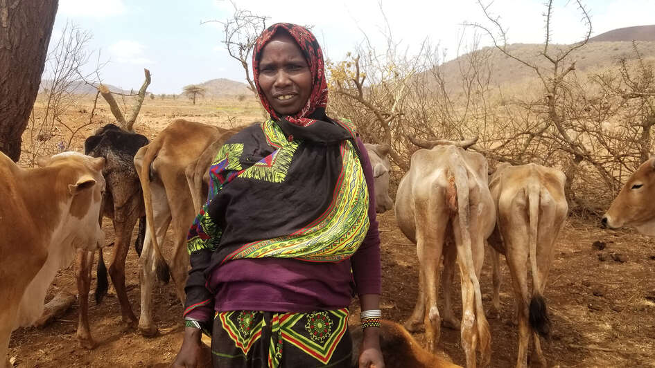 Eine Frau steht vor ihrem abgemagerten Vieh.