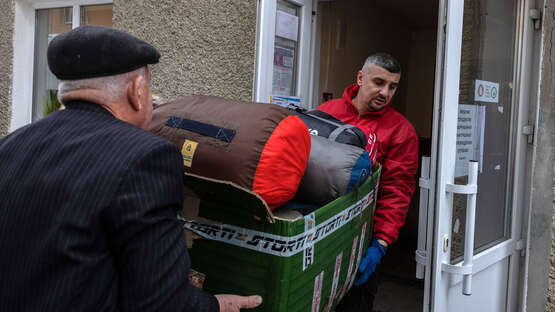 Zwei Männer tragen eine Kiste voller Schlafsäcke in ein Gebäude.