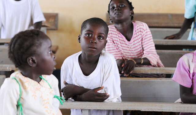 Kinder sitzen hintereinander in Schulbänken