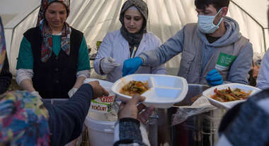 Zwei Frauen und ein Mann stehen in einem Zelt und verteilen Mahlzeiten.