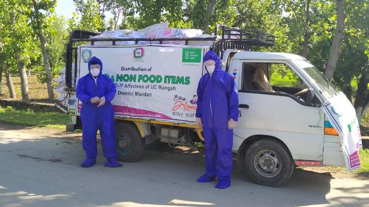Zwei Männer in Schutzausrüstung stehen vor einem Kleinbus der Welthungerhilfe.