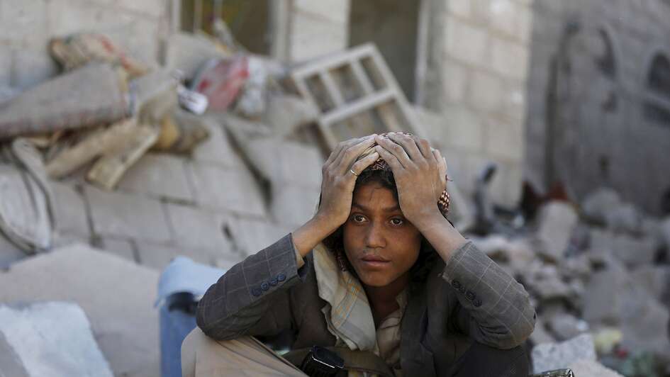A young man sits next to a heap of rubble.