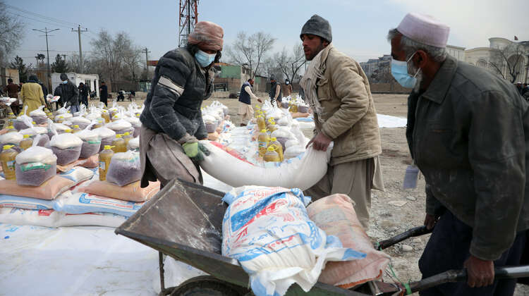 Zwei Männer laden einen Sack Mehl auf eine Schubkarre. 