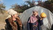 Zwei Frauen stehen vor einem Gewächshause. Eine hält einen Kürbis in der Hand, Tadschikistan 2021.