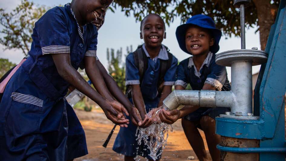Kinder waschen sich an einem Brunnen die Hände.