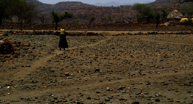 Ein Kind holt Wasser mit einem Kanister und geht durch eine ausgetrocknete Landschaft.