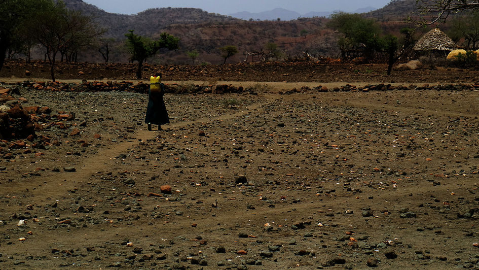 Ein Kind holt Wasser mit einem Kanister und geht durch eine ausgetrocknete Landschaft.