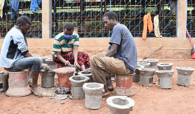 Drei junge Menschen sitzen sich gegenüber und töpfern Öfen, Burundi 2021 