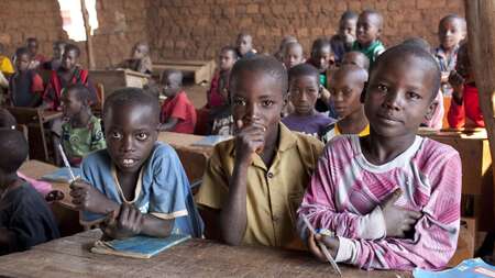 Drei Jungen sitzen im Vordergrund einer Schulklasse in Burundi