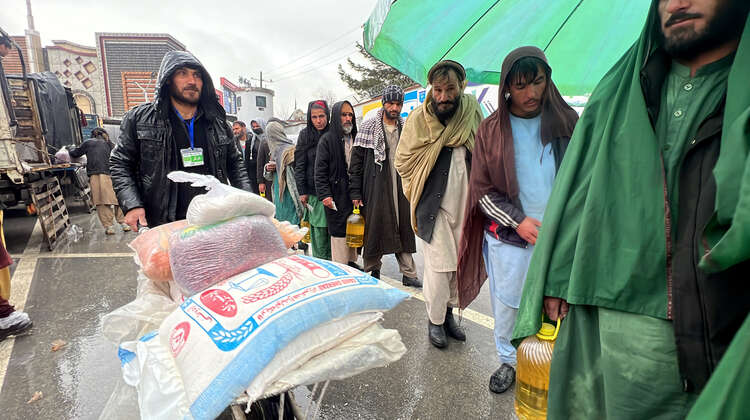 Lebensmittelverteilung in Kabul: Männer stehen Schlange, während ein Mann mit einer Schubkarre Säcke mit Bohnen und anderen Lebensmitteln vorbei schiebt. 