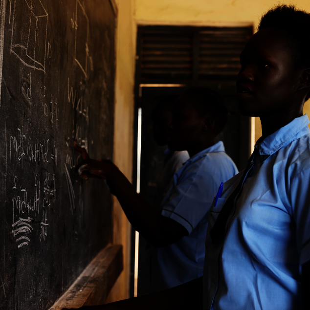 Bild aus einem Projekt im Südsudan mit Schulspeisungen, ein Mädchen steht an einer Schultafel.