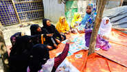 Rohingya women sitting on the floor looking and pointing at hygiene training cards