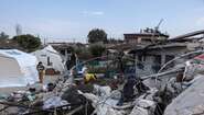 Ein altes und durchs Erdbeben zerstörtes Haus steht neben neu aufgebauten Zelten.