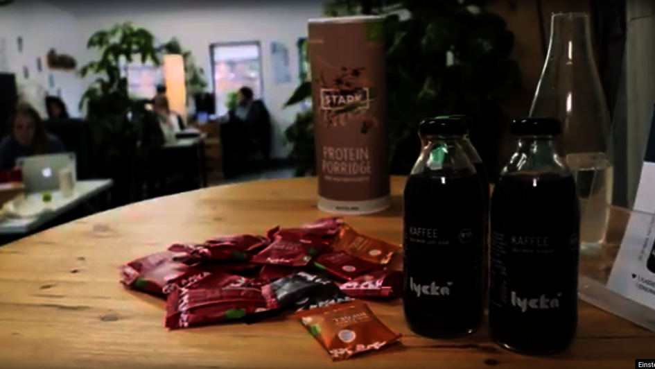 zwei Flaschen Lycka Kaffe stehen auf einem Holztisch. Im Hintergrund ist ein Café zu sehen.