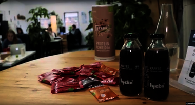 zwei Flaschen Lycka Kaffe stehen auf einem Holztisch. Im Hintergrund ist ein Café zu sehen.