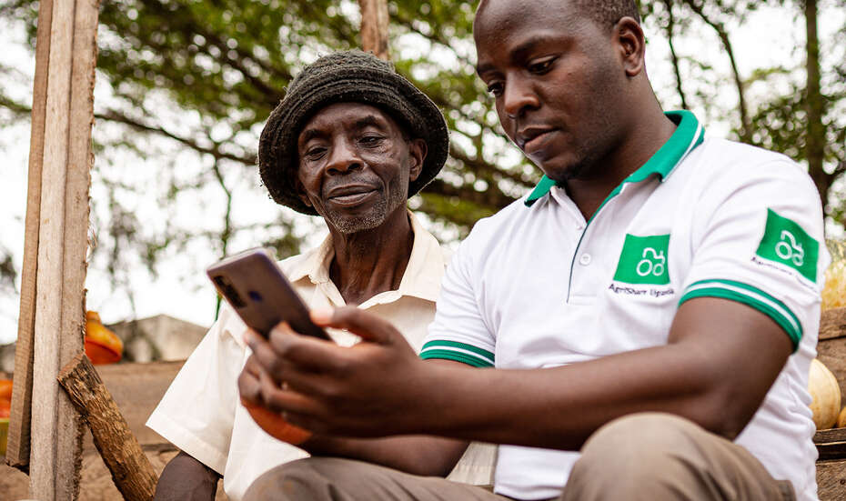 Two smallholder farmers look at their smartphones and engage with the agricultural app AgriShare, Uganda 2021.
