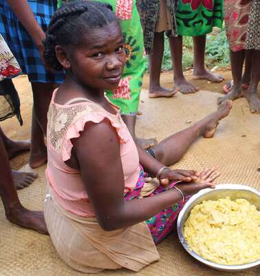 Two women sit on the floor with a bowl full of dough and prepare food.