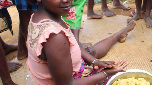 Two women sit on the floor with a bowl full of dough and prepare food.