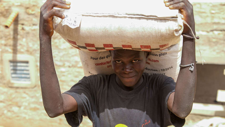 Ein Mann bei einer Nahrungsmittelverteilung hält einen großen Sack auf Kopf und Schultern. 