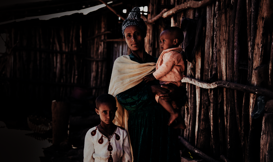 Eine Mutter mit ihren beiden Kindern; eines trägt sie auf dem Arm.