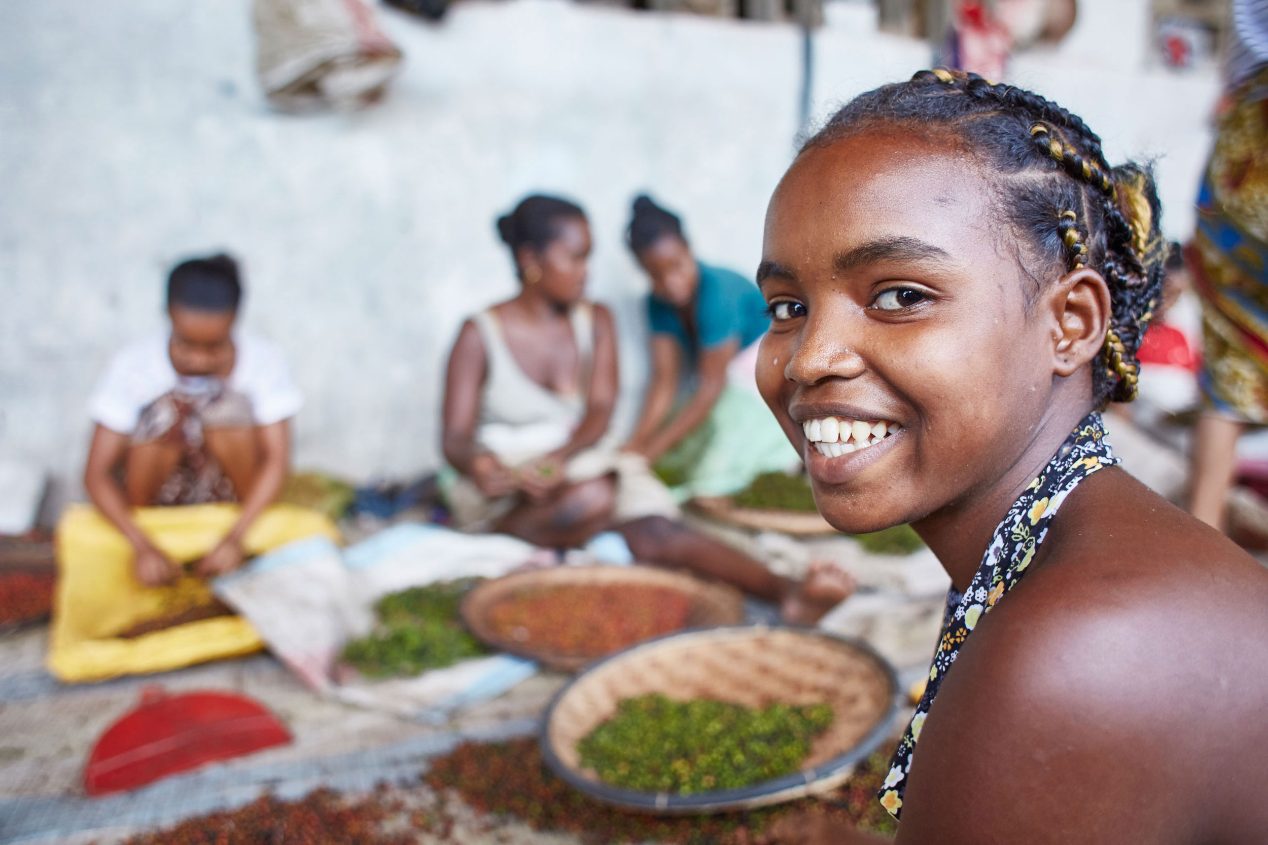 Mädchen und Frauen arbeiten in einer Pfefferfabrik, ein Mädchen im Vordergrund lächelt in die Kamera
